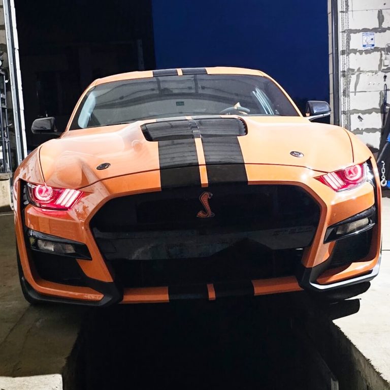 Oranžinis „Ford Mustang“ su kobros simboliais priekiniuose žibintuose ir grotelėse