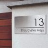 Sidabro spalvos adreso lentelė „Draugystės Alėja 13“ ant fasado.