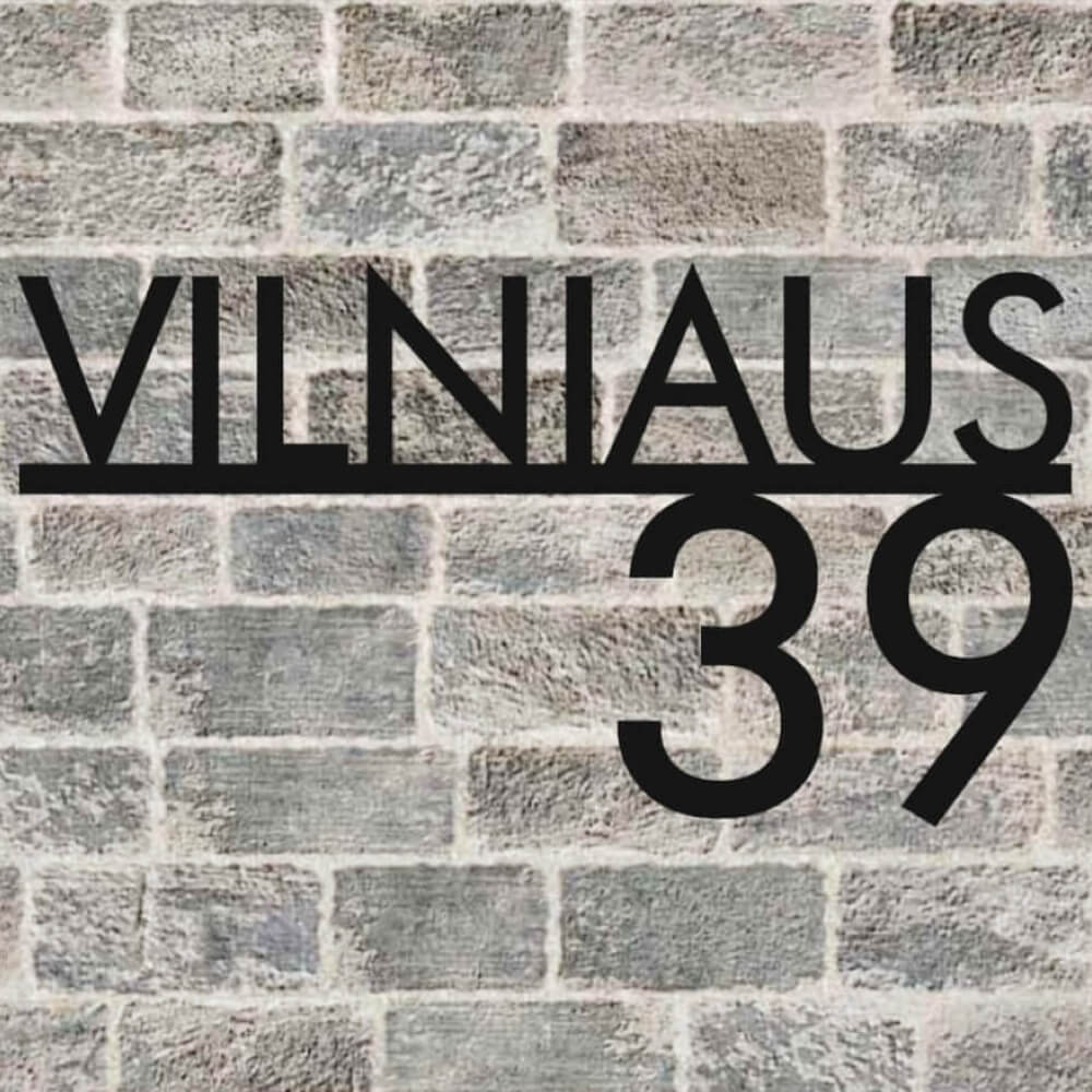 Juodas išpjautas užrašas „Vilniaus 39“ ant plytų sienos.