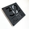 Juoda adreso lentelė „P. Lukšio 32“ su iškiliais tamsiais simboliais.