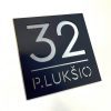Juoda adreso lentelė „P. Lukšio 32“ su sidabro spalvos simboliais.