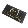 Juoda adreso lentelė „Ožiarūčių 6-1“ su aukso spalvos simboliais.
