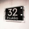 Skaidri adreso lentelė „P. Lukšio 32“ su juodu lauku ir distanciniais laikikliais.