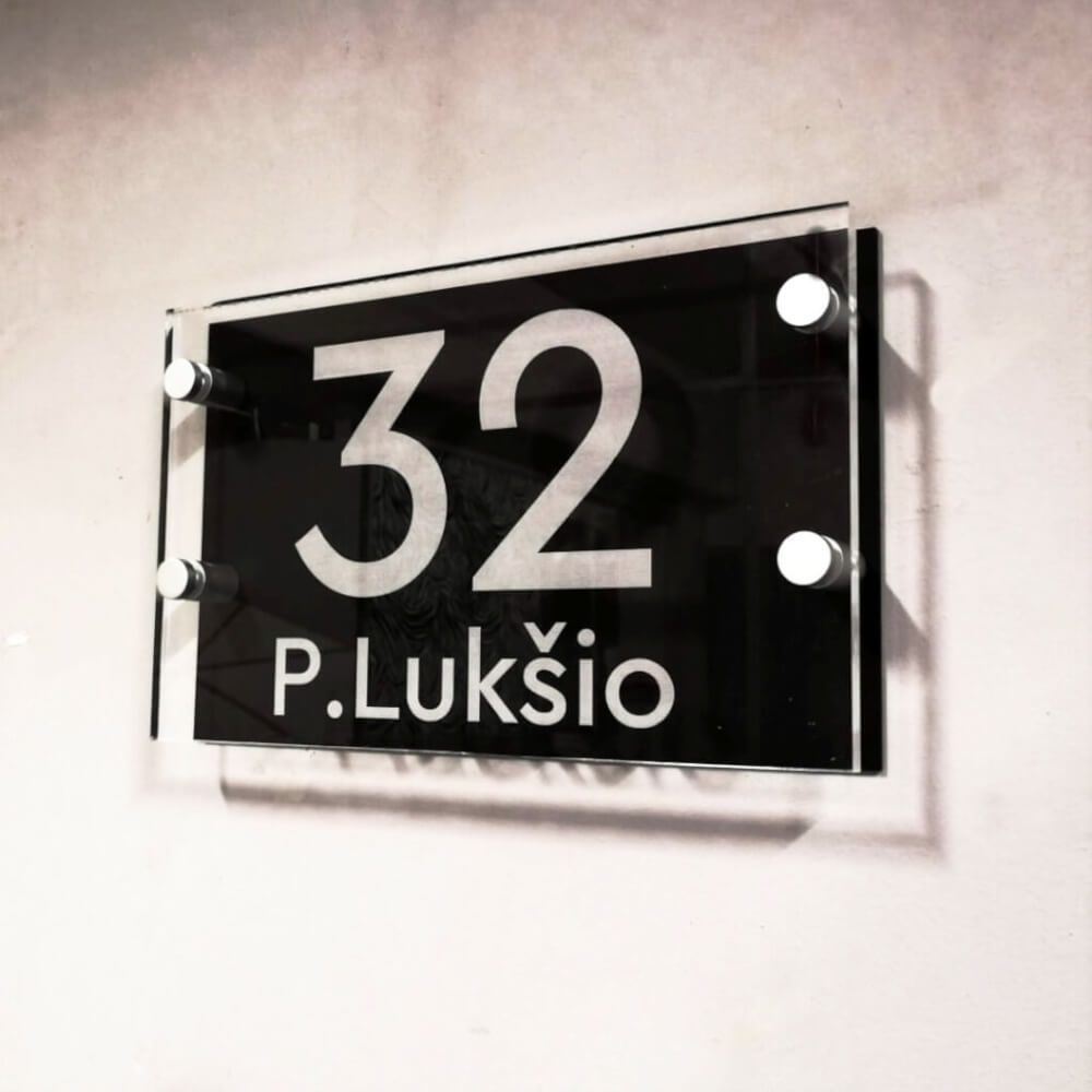 Skaidri adreso lentelė „P. Lukšio 32“ su juodu lauku ir distanciniais laikikliais.