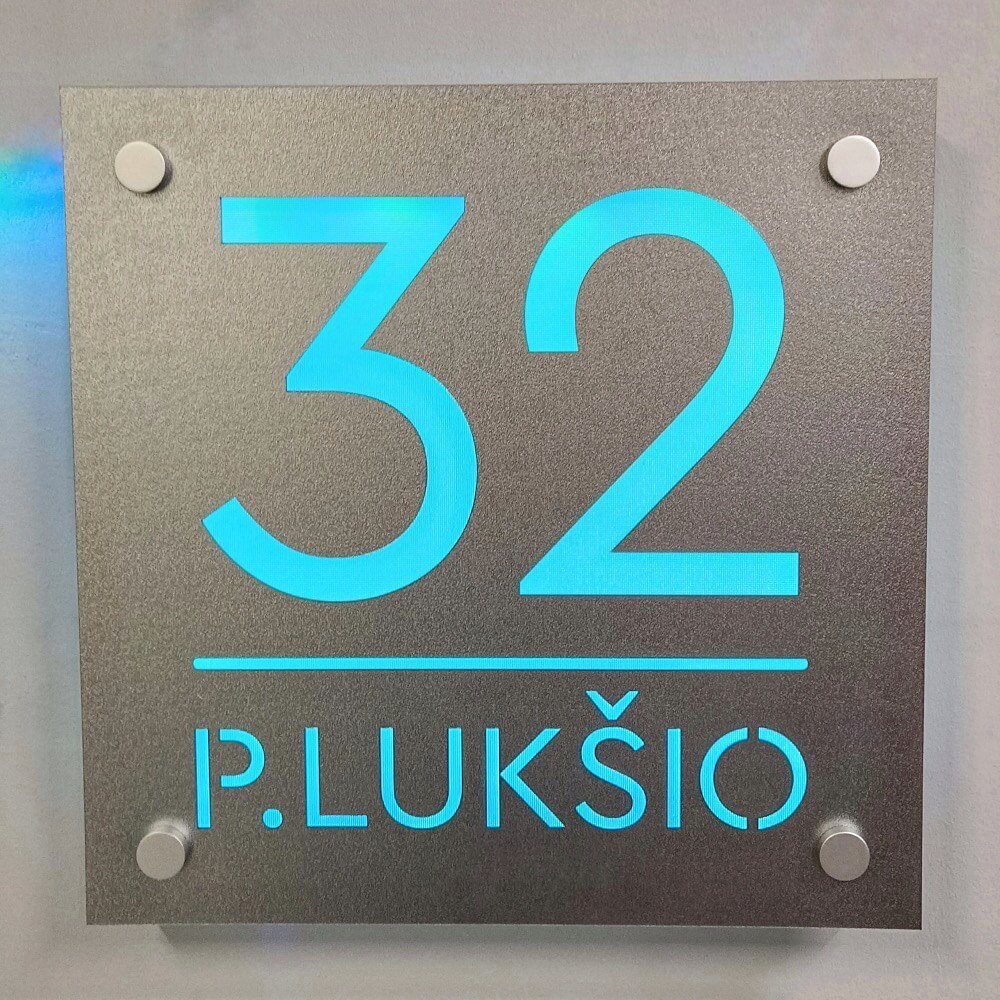 Sidabro spalvos adreso lentelė „P. Lukšio 32“ su turkio spalva šviečiančiais simboliais.