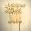Aukso spalvos 90-mečio torto smeigtukas su užrašu „Mylimai senelei“ ir ornamentais.