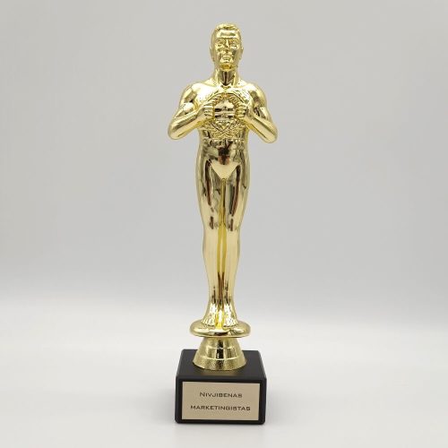 Aukso spalvos žmogaus figūros statulėlė su nominacijos lentele ant juodo pagrindo.