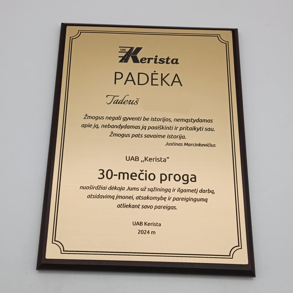Aukso atspalvio padėkos plaketė už ilgametį darbą tamsiame rėmelyje.