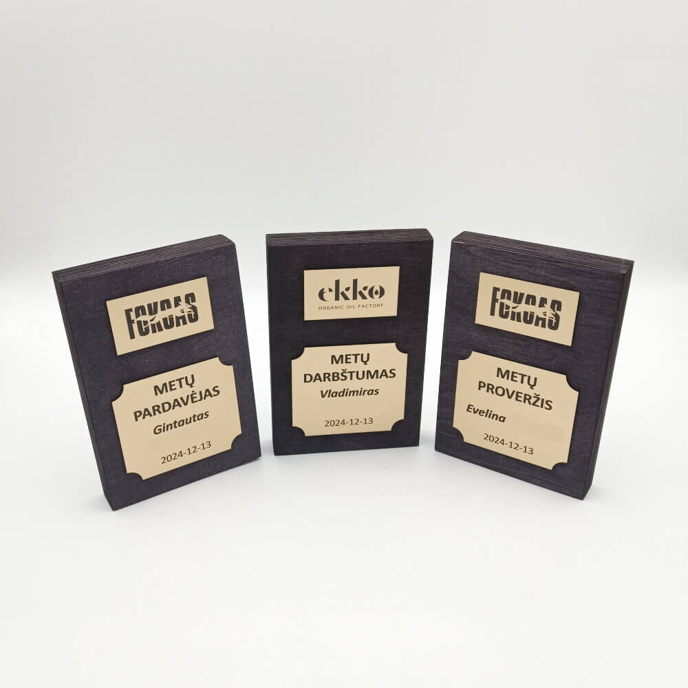 Trys tamsios stačiakampės plaketės su aukso spalvos darbuotojų nominacijomis.