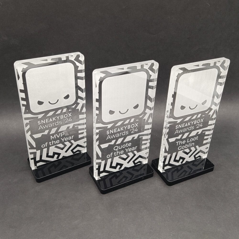 Trys stilizuotos Sneakybox Awards apdovanojimų statulėlės ant juodų pagrindų