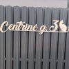 Išpjautas gatvės užrašas „Centrinė g. 3“ su katino siluetu ant tvoros.