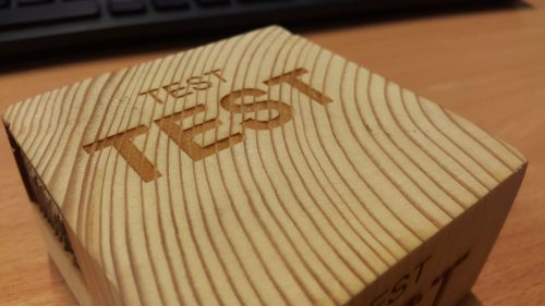 Užrašai „TEST“ išgraviruoti ryškiai rievėtame mediniame ruošinyje