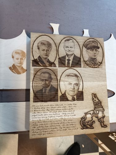 Penki portretai ir tekstas išgraviruoti rievėtoje medžio plokštėje