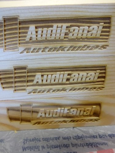 Trys „AudiFanai Autoklubas“ logotipo graviūros su matomomis rievėmis įgilintame fone