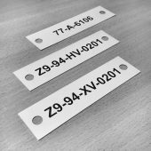 Trys siauros metalinės identifikavimo lentelės su numeriais ir tvirtinimo angomis