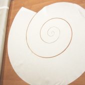 Lazeriu išpjauta spiralė baltame sintetiniame audinyje.